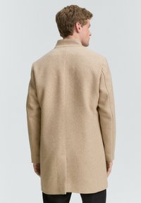 Beige wollen jas met een rechte snit, voorzien van een kraag en lange mouwen, vanuit de rug getoond tegen een lichte achtergrond.