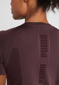 Lyhythihainen viininpunainen urheilupaita, jossa on teksturoidut yksityiskohdat ja Puma-logo takana. Paita on istuva ja hengittävä.