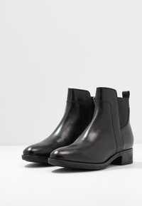Botas de cuero negro hasta el tobillo con un acabado suave, paneles laterales elásticos y un tacón bajo en bloques. Presentan una cremallera y líneas simples y limpias.