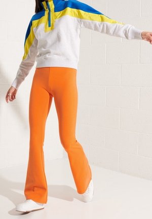 Maglione grigio e blu con zip e dettagli gialli, abbinato a leggings arancioni a campana e sneakers bianche. Tessuti morbidi.