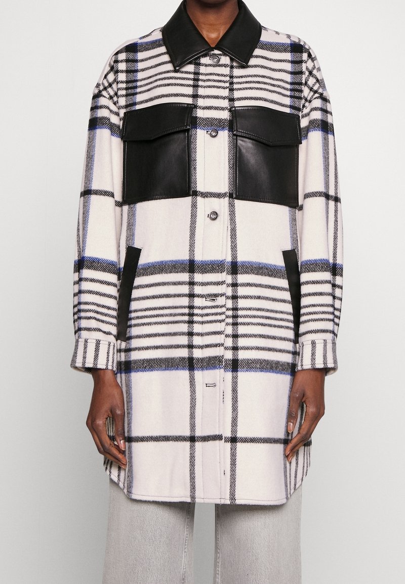 Checkered oversized coat with black leather accents, featuring large front pockets, buttons, and a contrasting collar. Soft fabric texture.