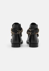 Botas de tobillo de cuero negro con un tacón bajo, que presentan acentos de cadena dorada alrededor del tobillo y un detalle de hebilla en el lateral.