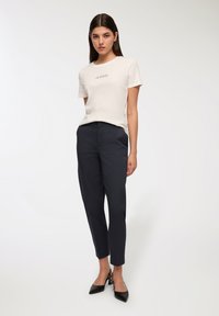 Kremowa koszulka z krótkim rękawem z nadrukiem tekstu, w zestawieniu z ciemnonawowymi spodniami w kant oraz czarnymi szpilkami. Gładkie tekstury tkanin.