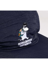 Meripartiohattu, joka on valmistettu teksturoidusta kankaasta ja jossa on brodeerattu Moomin-hahmo, jolla on reppu ja päällysmyssy, sekä teksti "NORDICBUDDIES CLOTHING CO."