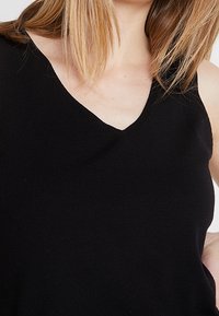 Black, sleeveless top with a V-neck design, made from a soft, stretchy fabric. Features a smooth texture and subtle stitching details.