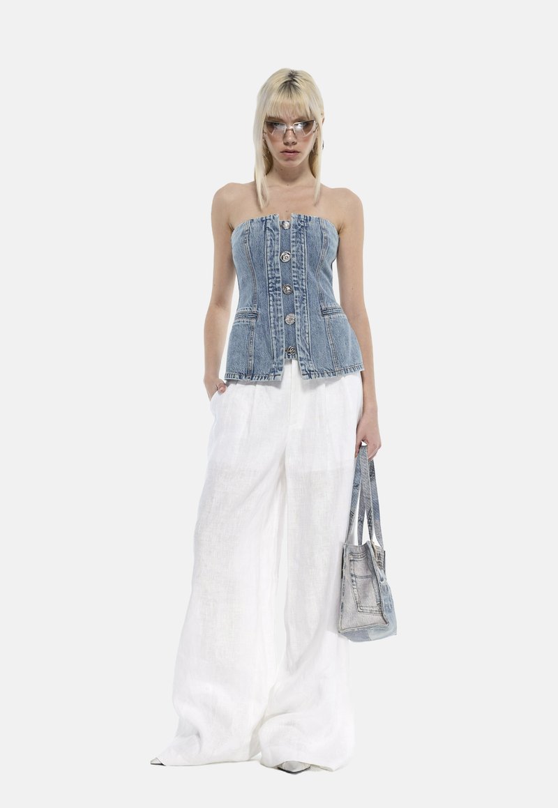 Top in denim senza spalline con bottoni frontali, abbinato a pantaloni larghi in lino bianco e una piccola borsa in denim. Modella che indossa occhiali da sole trasparenti.