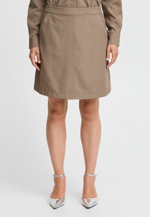 Bruine knie-lange rok met een zachte textuur, voorzien van zijzakken en een lichte flare. In combinatie met puntige zilveren hakken.