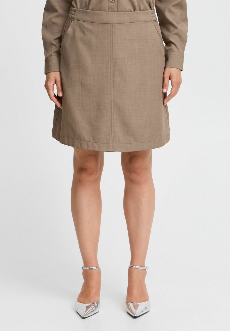 Jupe marron jusqu'aux genoux avec une texture lisse, dotée de poches latérales et d'un léger évasement. Associée à des talons argentés pointus.