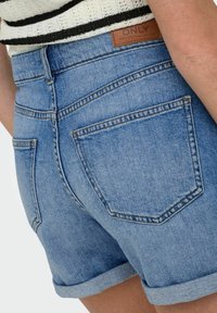 Shorts in denim blu chiaro con orlo sfrangiato, dotati di due tasche posteriori e un'etichetta in pelle marrone con logo in vita.