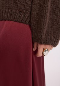 Brązowy sweter o dzianinowej fakturze, w połączeniu z burgundową spódnicą. Metalowy pierścień podkreśla rękę.