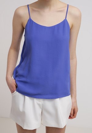 Cami-top in een levendige blauwe kleur, gemaakt van gladde stof, met dunne bandjes en een relaxte pasvorm. Gecombineerd met witte shorts, wat een casual uitstraling geeft.