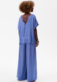 Pantalons larges bleu clair associés à un haut assorti avec un dos en V et des liens. Tissu lisse avec une coupe décontractée.