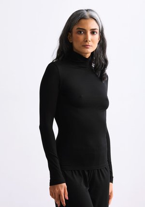 Schwarzer Rollkragenpullover mit schmal geschnittenem Design und langen Ärmeln aus glattem Stoff, kombiniert mit schwarzen Hosen.