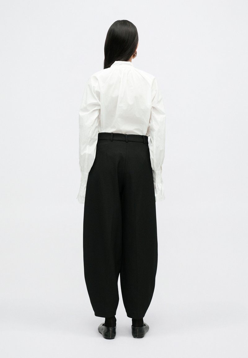 Camicia bianca con maniche a sbuffo, pantaloni neri a vita alta, scarpe nere, tessuto liscio, vestibilità morbida e design minimalista.