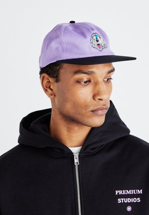 Man draagt een lavendel- en zwarte pet met een hond met kleurrijke geborduurde bril, zwarte hoodie met ritssluiting en de tekst "Premium Studios".