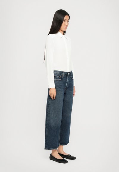 White long-sleeve button-up shirt paired with dark blue wide-leg jeans and black flats. Smooth fabric and casual fit.