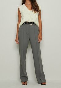 Un pull sans manches en tricot vert clair associé à un pantalon gris large taille haute, rehaussé par une ceinture noire.