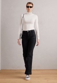 Black high-waisted jeans with a flared design, paired with a white long-sleeve turtleneck and silver sneakers. Accessories include sunglasses.