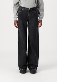 Black wide-leg jeans made of denim, featuring a high waist, front pockets, and a button closure, paired with black platform shoes.