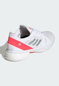White athletic shoe with a textured upper, pink accent stripe, and gray logo details; features a cushioned, rounded sole.