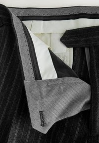 Black striped suit jacket interior featuring a herringbone pattern lining, light fabric, and black leather accents on the pockets.