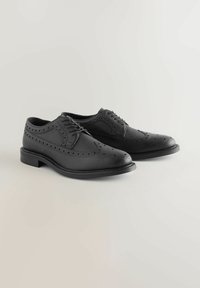 Chaussures habillées en cuir noir avec des détails en brogue, présentant un bout arrondi et un talon bas, une fermeture à lacets, et une finition texturée.