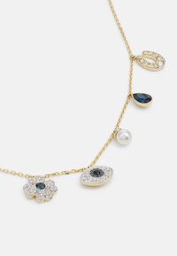 Zlatý náhrdelník s pěti přívěsky: perla, modrá slza, květina s modrým středem a dva motivy oka se třpytivými akcenty.