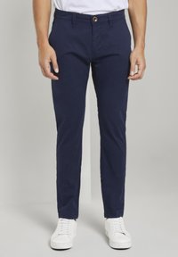 Námořnické modré chinos kalhoty se slim fit střihem, s knoflíkovým zapínáním a přední kapsou. Spárované s bílými teniskami pro neformální vzhled.