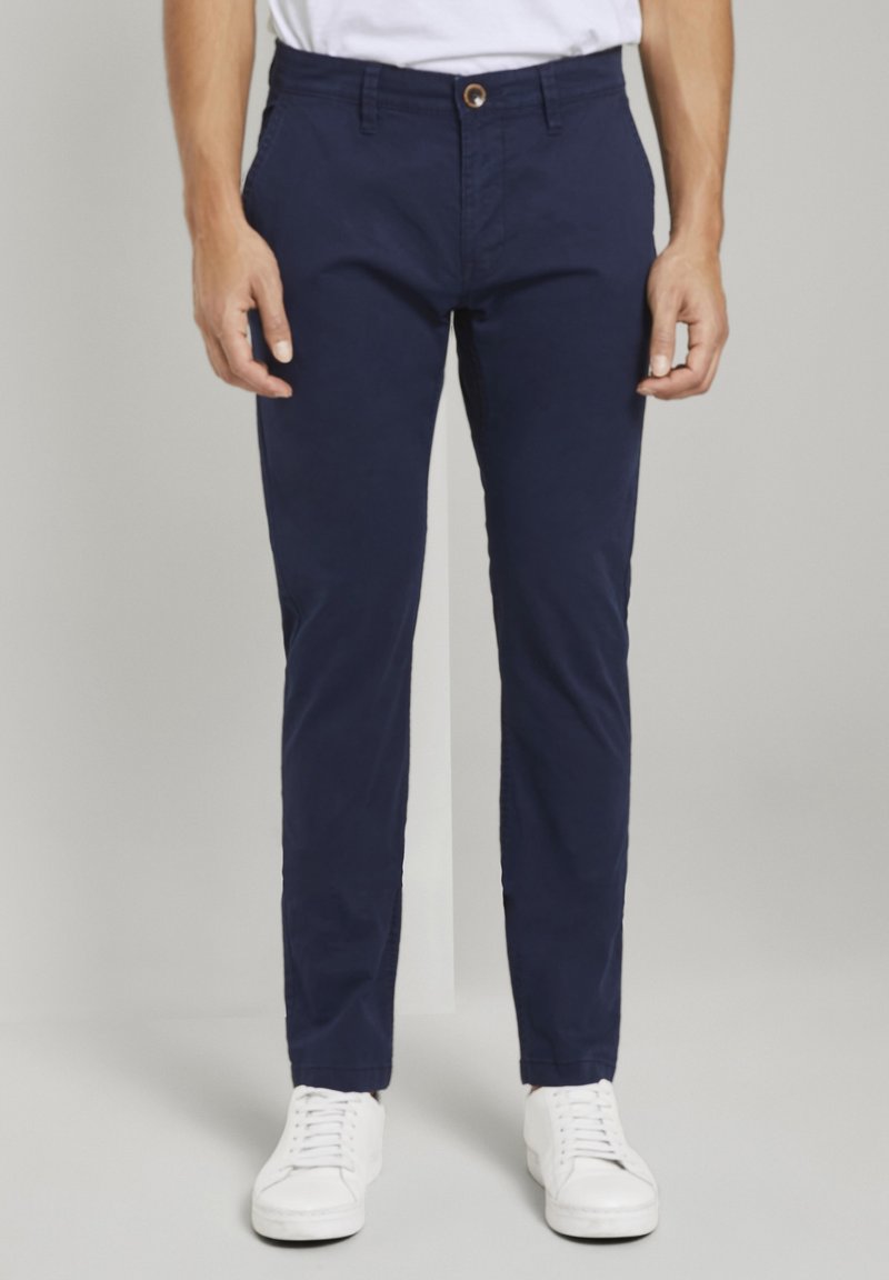 Námořnické modré chinos kalhoty se slim fit střihem, s knoflíkovým zapínáním a přední kapsou. Spárované s bílými teniskami pro neformální vzhled.