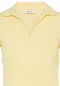 Haut en maille jaune pâle à manches courtes avec un col et une ouverture en V, présentant un motif texturé subtil.