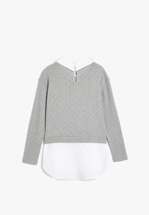 Harmaa neule, jossa on teksturoitu timanttikuosi, valkoinen kaulus ja avoin selkäosa. Kerrostettu valkoisen paidan helman päälle. Pitkät hihat.