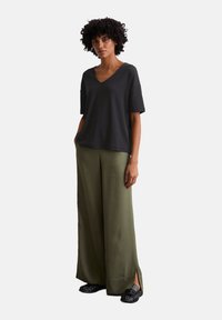 Black short-sleeve v-neck t-shirt paired with loose olive green wide-leg pants and flat black shoes, featuring side slits on the trousers.