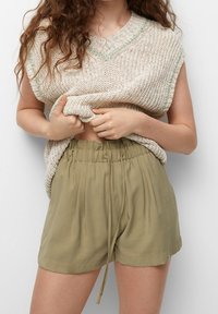 Gebreid beige mouwloos shirt met een V-hals en groene accenten, gecombineerd met olijfgroene shorts met trekkoord. Beide kledingstukken hebben een relaxte pasvorm.