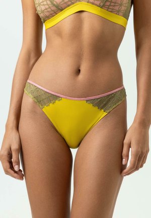 Vrouw die gele bikinibroekjes draagt met groene kanten zijkanten en roze rand, en bijpassende kanten bikinitop met gele band.