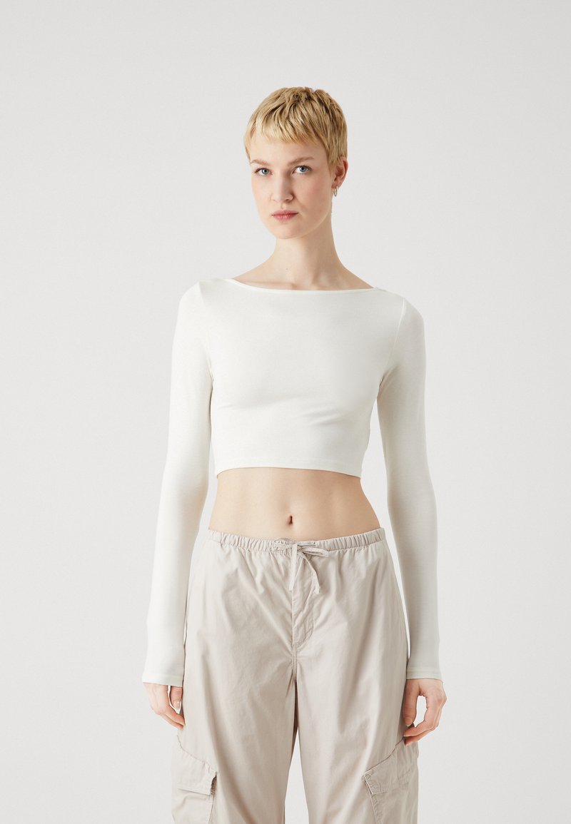 Top cropped alb, cu maneci lungi, dintr-un material neted și elastic; asociat cu pantaloni cargo bej, cu talie elastică, având buzunare laterale.