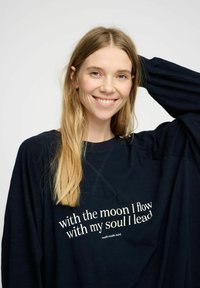 Felpa oversize blu navy con scollo rotondo e maniche lunghe, adornata da testo bianco che recita "con la luna fluisco con la mia anima guido."