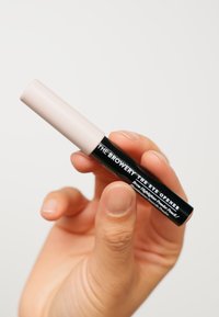 Ein schwarzer und hellrosa Augenbrauen-Highlighter-Stift, der in einer Hand gehalten wird, mit klarer Markenbeschriftung auf der Seite und einem glatten, zylindrischen Design.