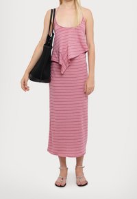 Abito a righe rosa con top a strati svasato, gonna aderente e spalline sottili. Completato da una borsa a tracolla nera con texture e sandali argento.