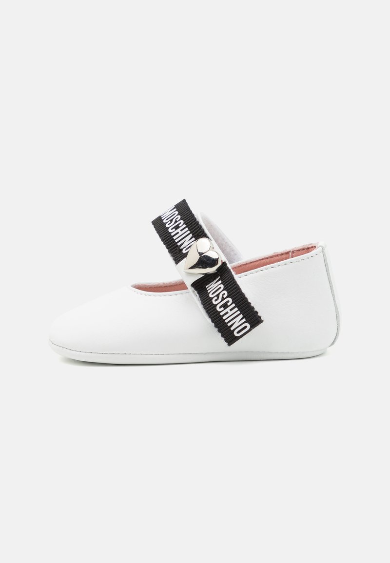 Bílé kožené boty s kulatou špičkou, které mají černý elastický pásek s textem "MOSCHINO" a stříbrným srdíčkovým akcentem.