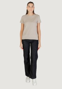 T-shirt beige con testo luccicante "Guess Los Angeles", abbinata a jeans scuri e sneakers bianche con plateau. Design semplice e informale.