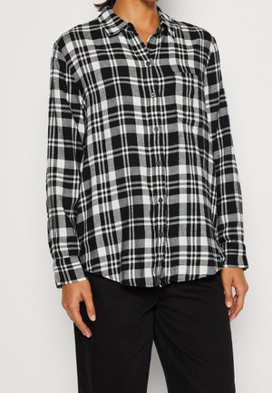 Camisa de franela de cuadros en blanco y negro con mangas largas, botón frontal y bolsillo en el pecho, que presenta un ajuste relajado y una textura suave.