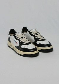 Sneaker in pelle bianca e nera con design perforato, lacci beige e il testo "GAME SET MATCH" sul lato. Suola in gomma.