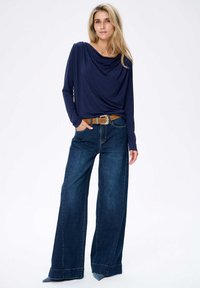 Navy-blaues, langärmeliges Oberteil, kombiniert mit übergroßen blauen Denim-Jeans, die einen braunen Ledergürtel und dezente Nahtdetails aufweisen.