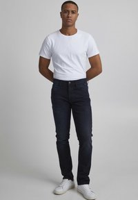 Jeans de mezclilla azul oscuro con un corte ajustado, combinados con una camiseta blanca ajustada. El atuendo se complementa con zapatillas blancas.