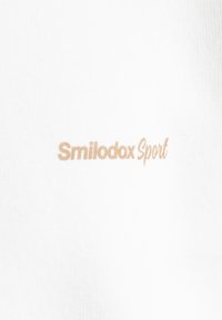 Tissu blanc arborant le texte "Smilodox Sport" en beige clair. Le matériau a une texture lisse avec un léger motif côtelé.