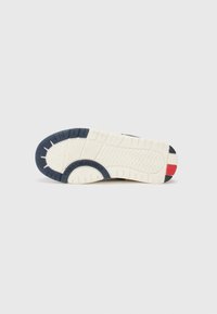Semelle de chaussure avec un fond en caoutchouc texturé, présentant des couleurs marine, blanche, avec des accents de rouge et noir ; comprend des détails de logo et un motif de semelle.