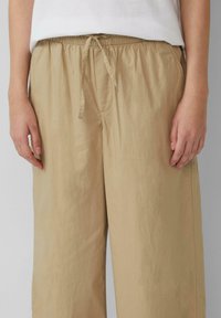 Beige, lichte broeken met een elastische tailleband, verstelbaar trekkoord en een losse pasvorm, met een subtiele textuur en minimalistisch design.