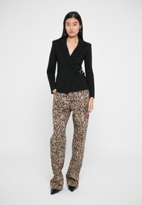 Blazer noir ajusté avec décolleté en V et détail de ceinture sur le côté, associé à un pantalon large en imprimé léopard beige et des escarpins noirs à bouts pointus.
