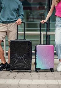 Dvoukolové cestovní kufry: černý kufr s vlnkovými vzory a kufr s gradientem růžové do modré, oba s tvrdým pouzdrem a teleskopickými rukojeťmi.