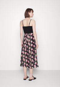 Top preto com alças finas combinado com uma saia maxi floral com flores cor-de-rosa sobre um fundo preto e um detalhe de cintura amarrada.